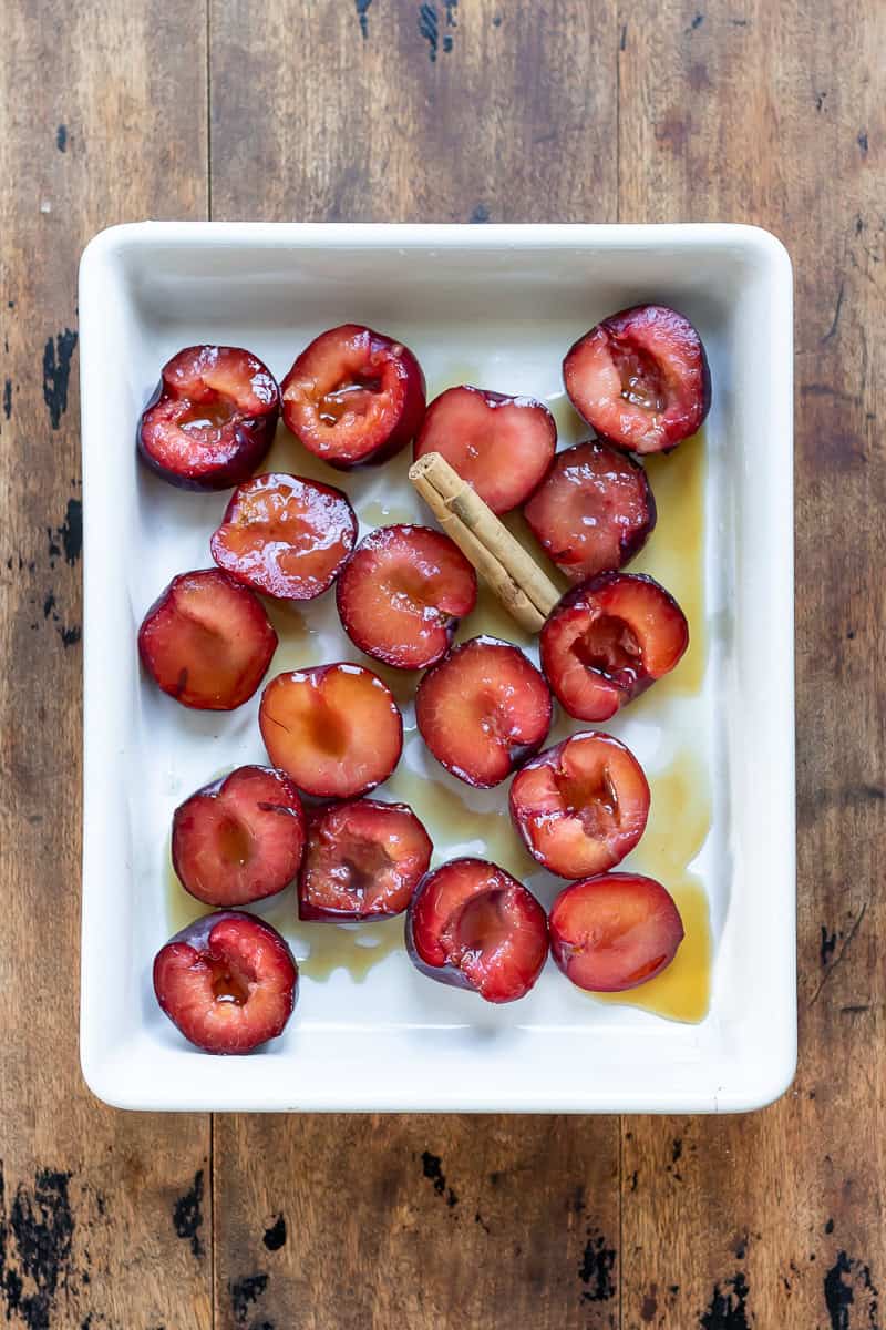 Plums in a baking dish with honey and a cinnamon stick.