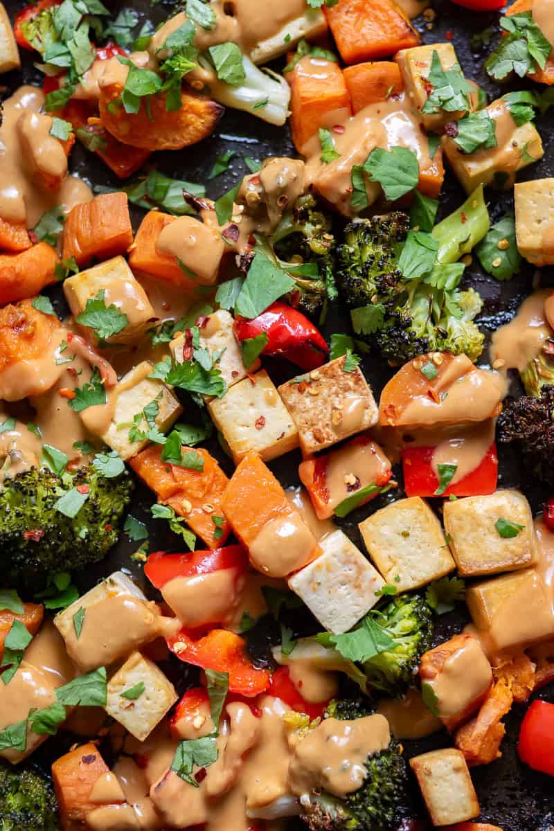 Sheet pan of roasted vegetables and tofu, drizzled with peanut lime sauce and sprinkled with chili flakes.
