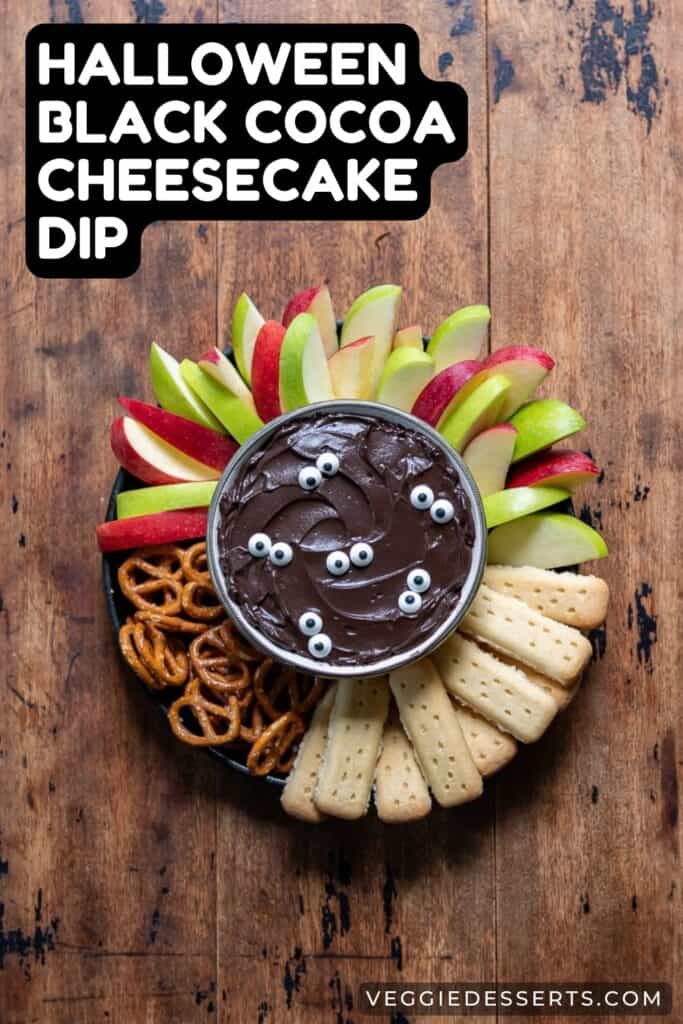 Dish of dip surrounded by sliced apples, pretzels and shortbread with title: Halloween Black Cocoa Cheesecake Dip.